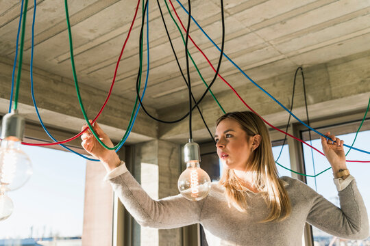 Young businesswoman in office examining cables at light bulbs