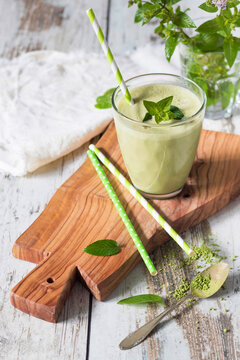 Glass of green smoothie with coconut milk, banana, matcha powder garnished with mint leaves