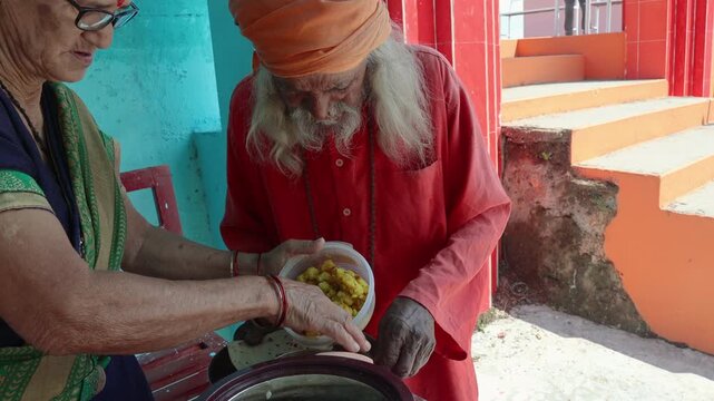 Raw video footage of an elderly woman serving traditional aloo ka gutka and roti to a Hindu sadhu at a temple in rural Uttarakhand, India. Spiritual charity and food sharing scene.