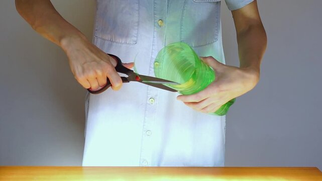 Woman refines cut edge of modified plastic bottle with scissors while finishing a handmade planter. Demonstrates functional object refinement, maker mindset workflows, and practical design adaptation.