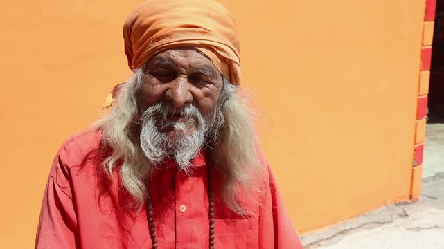 Raw video footage of an elderly Hindu sadhu with long white beard sitting near a temple in rural Uttarakhand, India. Spiritual atmosphere with traditional religious appearance.