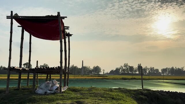 Scenic landscape of a temporary bamboo shelter next to an aquaculture fish pond during golden hour