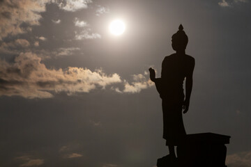 Obraz premium Silhouette of a Buddha statue against a bright sun and cloudy sky creating a peaceful spiritual atmosphere