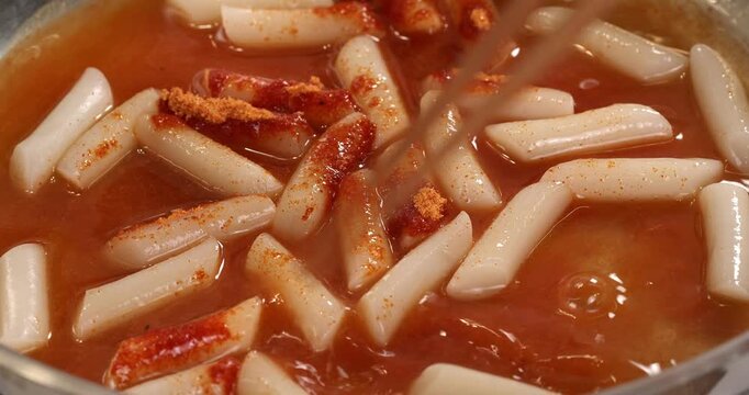 Process of cooking the Korean national dish tteokbokki. The tteokbokki are mixed with sauce in a pan.