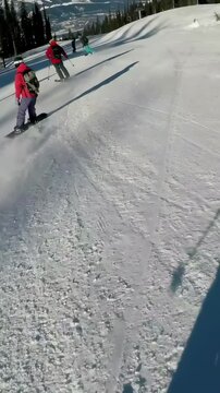 Vertical video: Chasing red snowboarder, skier filming behind as group descending on groomed run