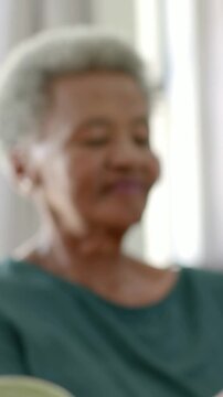 Vertical video: Pulling focus showing senior woman teal top checking phone at home plant left