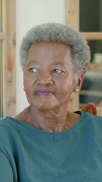 Vertical video: Hearing offscreen voice, senior woman in teal turning head on sofa, orange cushion