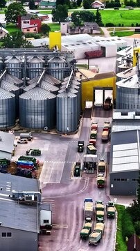Trucks queuing at a grain processing facility with large silos. Ideal for industrial or logistics themes.