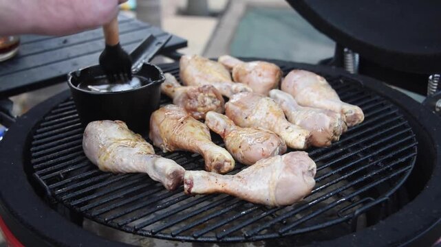 Male chef arranging and basting seasoned chicken drumsticks on a hot barbecue smoker. Preparing delicious grilled poultry for a summer party