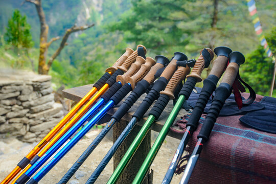 Row of colorful trekking poles on wooden table against blurred mountain background. Hiking and outdoor gear concept.