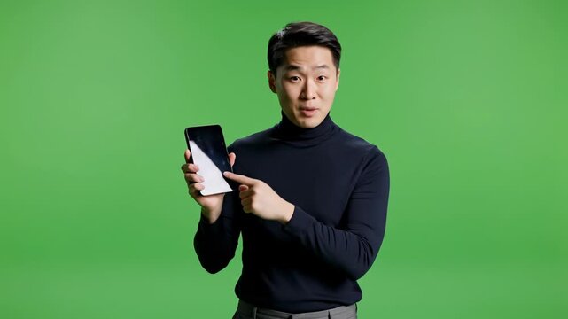 Young man holding smartphone in green screen studio portrait shot