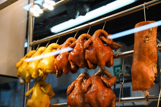 Close up of traditional Cantonese roasted duck chicken and crispy pork belly hanging in glass window display of street food restaurant