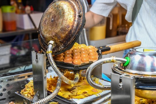 Baking traditional crispy bubble waffle in professional egg waffle maker machine at Temple Street Night Market street food stall in Hong Kong