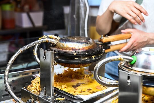 Baking traditional bubble waffles in professional egg waffle maker machines at Temple Street Night Market street food stall station in Hong Kong