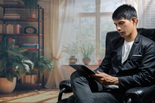 Young Man in Black Suit Sitting with Tablet in Cozy Indoor Setting