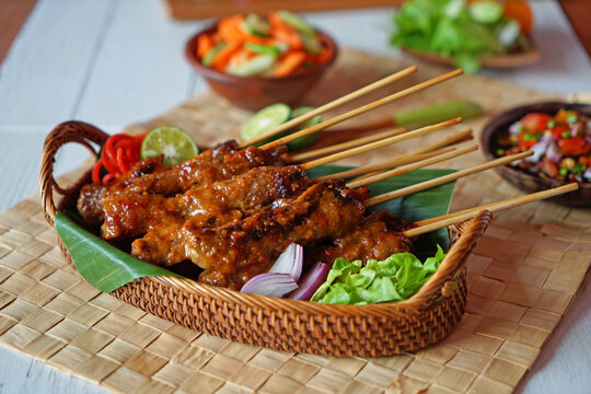 Traditional Indonesian chicken satay with peanut sauce served on bamboo skewers in a woven basket with fresh vegetables and sambal. Popular Southeast Asian street food with authentic Indonesian flavor