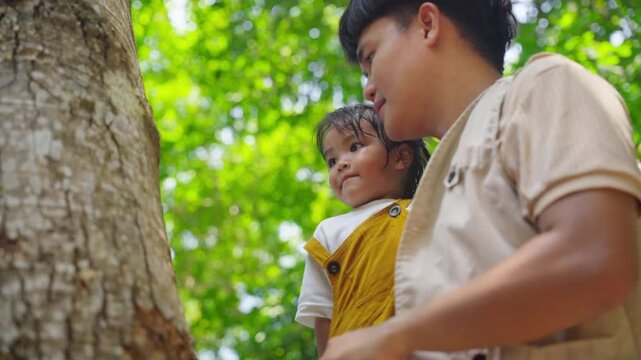 adventurAsian father teaching daughter using hands touching tree bark in forest, Parent guiding child nature exploration and environmental learning education outdoors adventure on summer holiday vacae