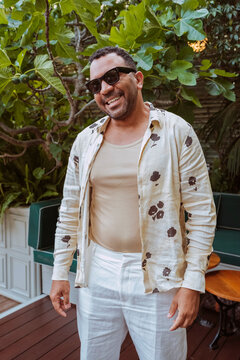 Latin american stylish man, smiles relaxing on a fig tree lined outdoor patio.