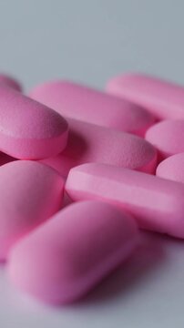 Vertical macro of rotating pink tablets on clean white background