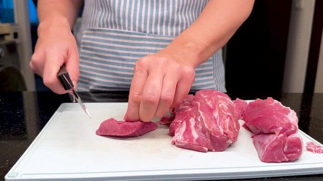 Woman trimming and slicing raw lamb meat on cutting board with knife. Real life video footage of cooking preparation, butchering meat, removing sinew and preparing fresh lamb in home kitchen.