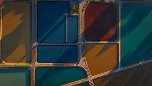 Aerial view of colorful industrial water treatment ponds with geometric shapes and different shades of blue, green, and brown water
