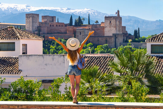 happy woman tourist with arms raised looking at alhambra fortress and sierra nevada mountains in granada spain