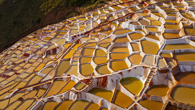 Aerial view of the maras salt mines in peru with thousands of ancient terraced pools filled with salty water reflecting the golden sunlight