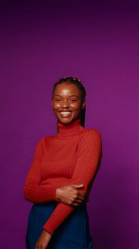 Confident young woman smiles and poses in a studio setting with vibrant colors. She's wearing stylish clothing.
