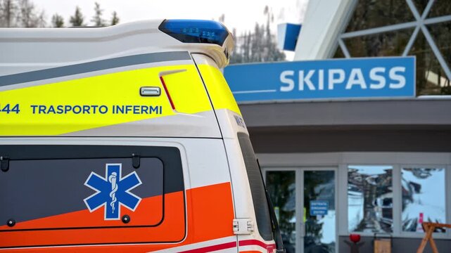 Ambulance parked outside a building with a ski pass sign, showcasing emergency services at a winter resort.