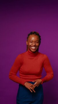 Young woman with colorful braids laughs heartily against a vibrant purple backdrop in a vertical medium shot