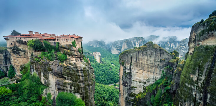 Amazing panoramic view with the majestic Varlaam Monastery amid creeping mists in the Meteora Valley near Kastraki, Greece