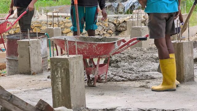 Construction workers transfer freshly mixed cement and sand mortar into a wheelbarrow at an active building site. Ideal for construction, masonry, teamwork, and infrastructure development concepts.