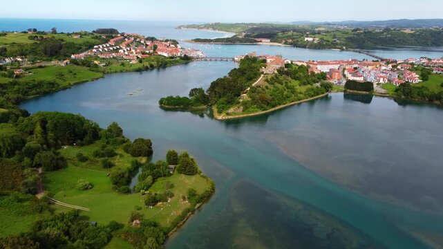 Wide aerial panoramic view of San Vicente de la Barquera estuary and coastline, featuring the green landscape, historic town and the Atlantic Ocean in Cantabria, Spain. High quality 4k footage