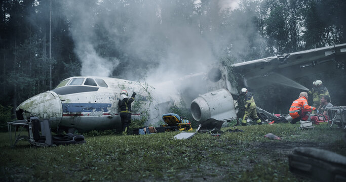 Firefighters and Paramedics Conduct Airplane Crash Rescue in a Smoky Forest, Treating Survivors Beside Damaged Fuselage Debris During Emergency Response and Firefighting Operations at Wreckage Site.