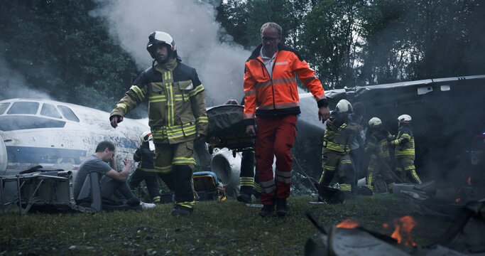Firefighters and Paramedics Work Through Heavy Smoke at an Airplane Crash Site, Searching Wreckage, Controlling Flames, and Rescuing Survivors Amid Scattered Debris in a Wooded Area After Impact.