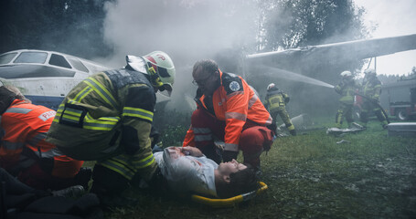 Firefighters and Paramedics Work Under a Smoke-filled Airplane Wing at a Forest Crash Site, Lifting...