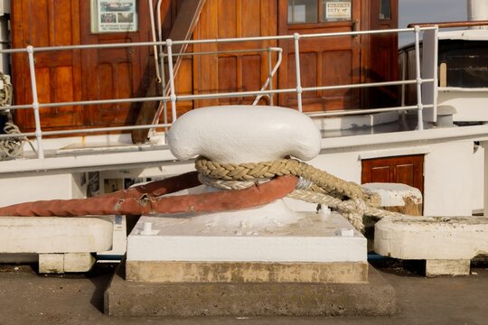 Thick mooring ropes and a red hose secured to a white bollard on the wharf in Auckland, New Zealand for a ship.