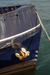 Obraz premium The bow of a dark blue ship, featuring a rusty metal anchor and draft markings, remains docked at a harbor in New Zealand.