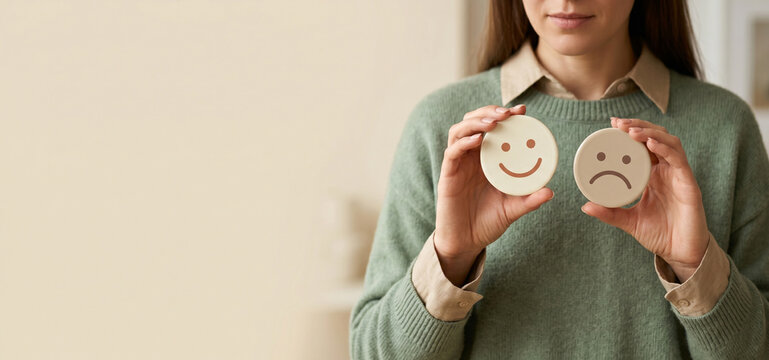 Person holding contrasting smiley and sad face icons representing mood swings and emotional balance