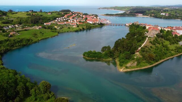 Wide aerial panoramic view of San Vicente de la Barquera estuary and coastline, featuring the green landscape, historic town and the Atlantic Ocean in Cantabria, Spain. High quality 4k footage