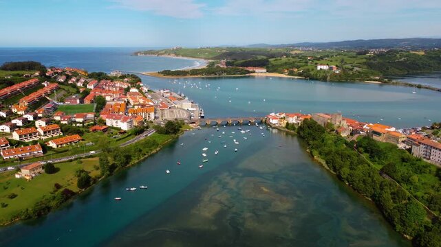 Wide aerial panoramic view of San Vicente de la Barquera estuary and coastline, featuring the green landscape, historic town and the Atlantic Ocean in Cantabria, Spain. High quality 4k footage