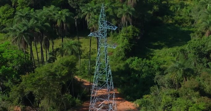Electric transmission tower corridor crossing Cerrado vegetation in Goi&aacute;s, Brazil, surrounded by tropical savanna woodland, palm species and fragmented native biome, aerial lateral tracking shot.