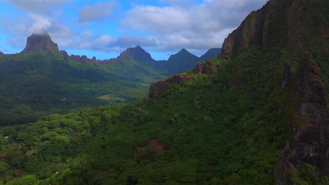 Dramatic volcanic jagged peaks rugged terrain Mount Rotui Mt Toheia Moorea French Polynesia aerial drone Belvedere Lookout landscape Cooks Opunohu Bay sunny morning blue sky low clouds circle right