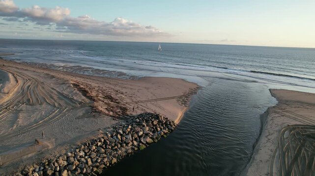 Aerial view of beach jetty sailboat and ocean waves on Southern California coast captured with smooth cinematic drone footage