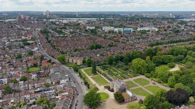 William Morris House and Lloyd Park, Walthamstow, London. Forward descending drone move over rooftops toward historic manor and green parkland on a bright day, establishing East London.