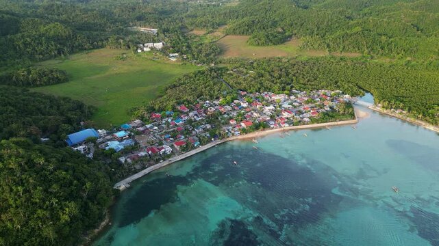 Aerial pullback over a rural coastal village, shallow reefs, lush hills, and clear waters - Magnesia Del Norte, Catanduanes, Philippines