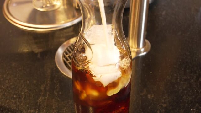 Fresh Milk Pouring Over Cold Brew Coffee in Glass Carafe Creating Creamy Swirl &mdash; Artisan Cold Brew Latte Preparation at Specialty Cafe Bar Station