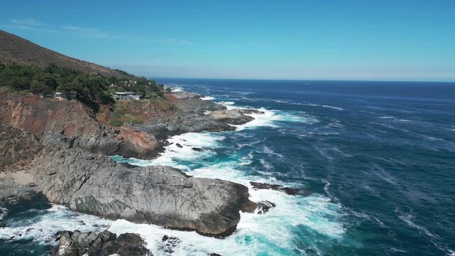 Advancing flight over exclusive clifftop villas with pools nestled into scrubland above secluded turquoise cove and dramatic rocky headland. Punta Pite, Papudo, Chile