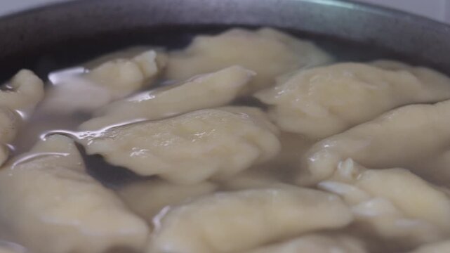 Close-up view of homemade pierogi or dumplings cooking in a large pot of boiling water, preparing a traditional Slavic meal.
