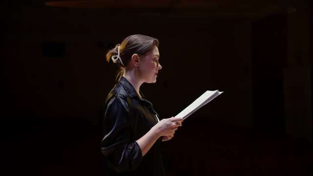 Actors rehearsing dramatic script in dimly lit theater, focused performers practicing lines and expressions during an intimate stage reading session
